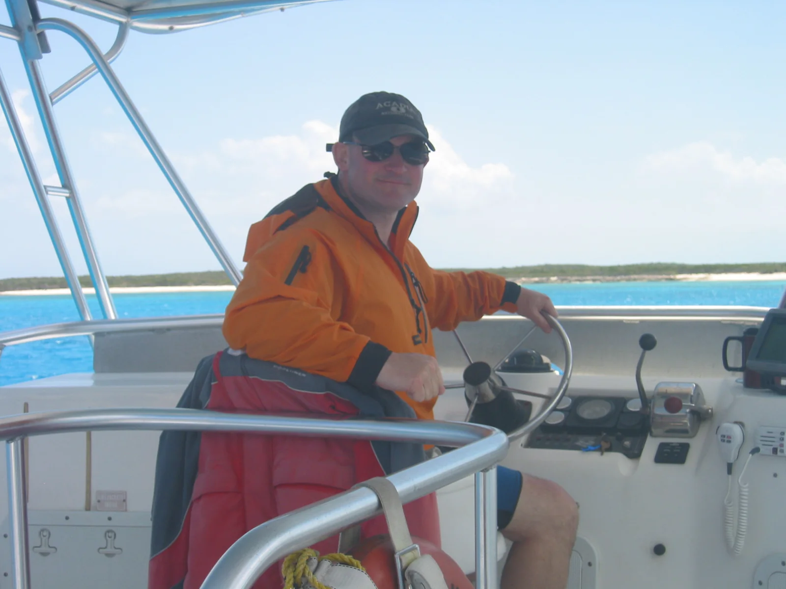 Scott in a cap and sunglasses at the wheel of a
                      small boat on bright turquoise water.