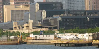 The West 30th Street Heliport pier seen from the
                        Hudson River, with helicopters on the pad and
                        the Javits Center behind it.