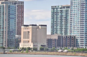 A Holland Tunnel ventilation building — a
                        blocky, building-sized tower with tall louvered
                        vents — seen from the water among Jersey City
                        high-rises.