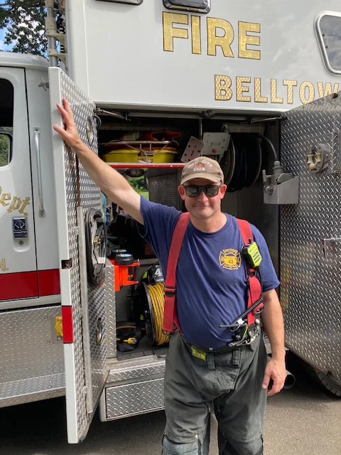 Scott in a Belltown Fire Department t-shirt and
                      radio harness, standing at the open equipment
                      compartments of the rescue truck.