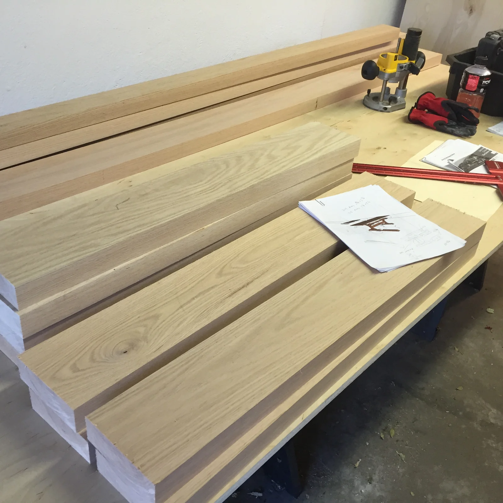 Milled oak boards stacked on a workbench with a
                    hand-drawn sketch of a trestle table, a router,
                    and layout tools.