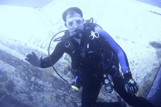 A scuba diver beside the fuselage of a sunken
                      airplane underwater.