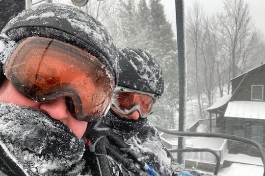 Two skiers, snow-covered head to toe, riding a
                      chairlift in a storm.